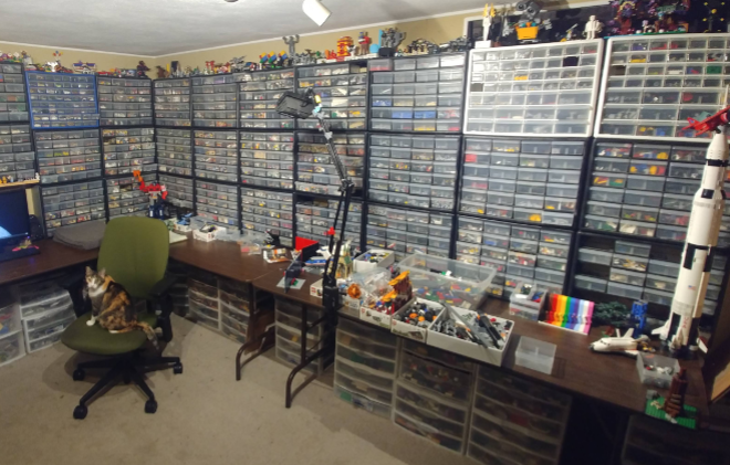 This image shows a home office with a computer, long tables, and hundreds of plastic drawers storing toy bricks pieces of varying colors, shapes, and sizes. A scale model of an Apollo-era Saturn V rocket sits upright next to a Space Shuttle orbiter. A cat with a golden brown calico coat sits on a green office chair in the center. Credit: NASA/JPL-Caltech/Stephen Pakbaz.