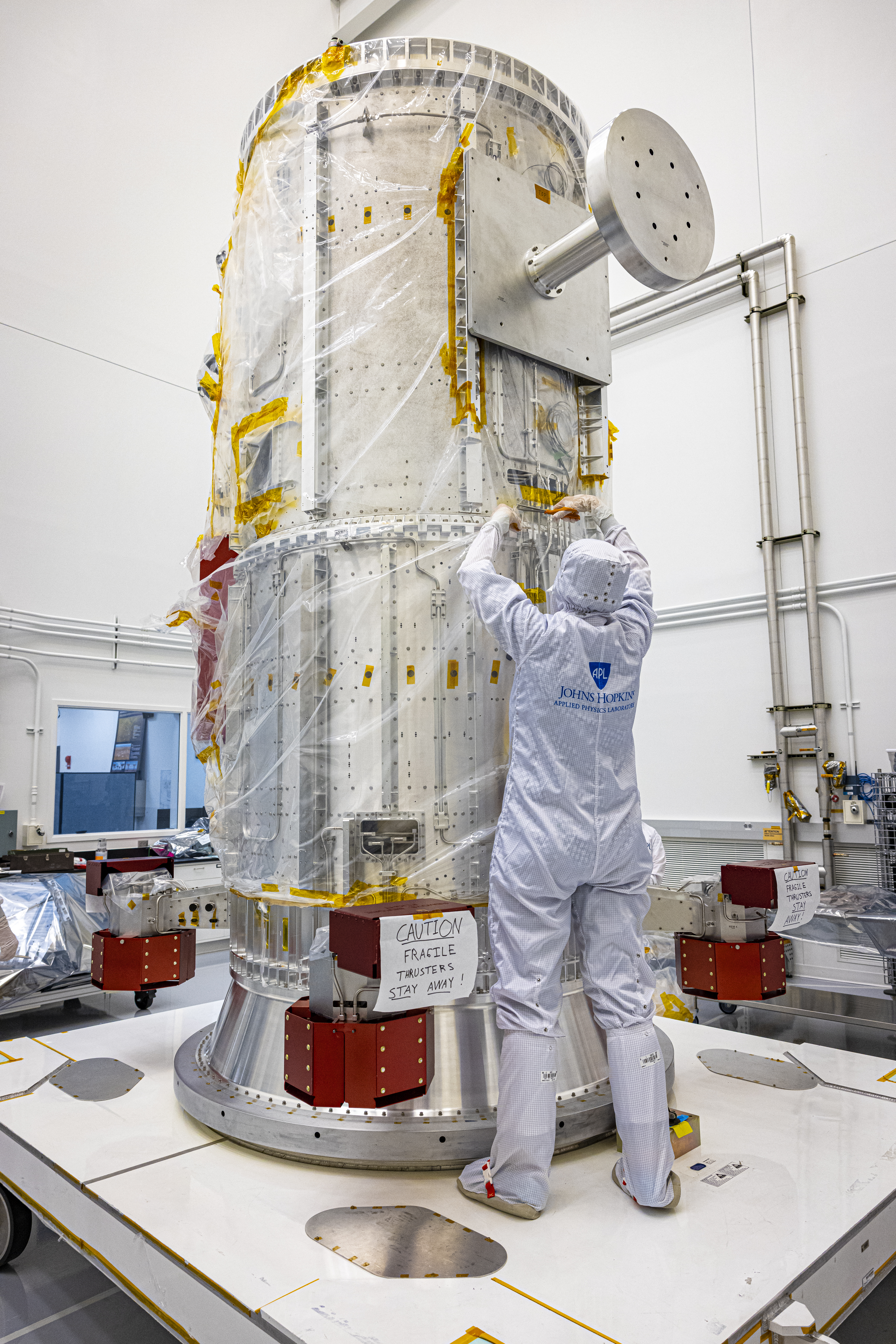 An engineer removes protective plastic wrap from Europa Clipper's propulsion module in a cleanroom.