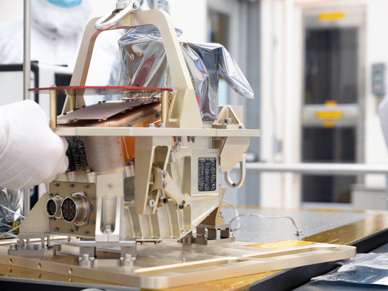 An engineer’s gloved hand on the casing holding the thermal imager instrument, located on a table in a clean room, preparing it for functional testing.
