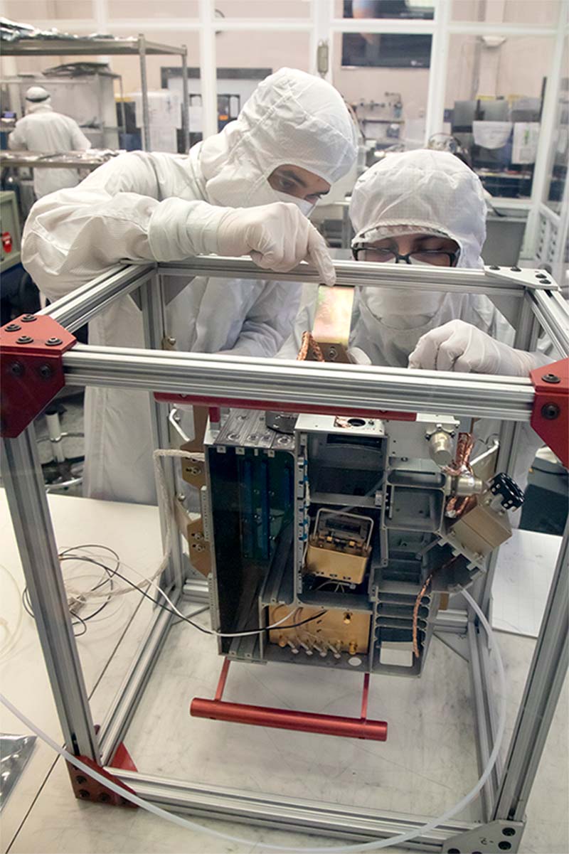 Southwest Research Institute (SwRI)’s Brandon Perez (mechanical engineer; left) and Bryan Esquivel (technician; right) prepare to install electrical boards into the Europa Ultraviolet Spectrograph (Europa-UVS) instrument, tipped up to show a top view. 