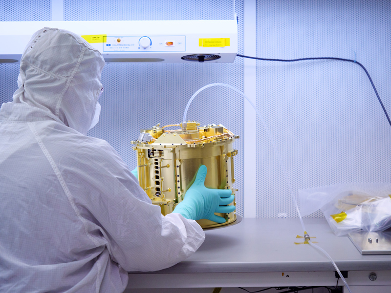 An image showing an engineer handles the SUrface Dust Analyzer (SUDA) in the clean room at the Laboratory for Atmospheric and Space Physics (LASP) at the University of Colorado Boulder. Dry nitrogen gas is continually pumped through the instrument during assembly and testing to ensure it remains clean and free of contaminants.