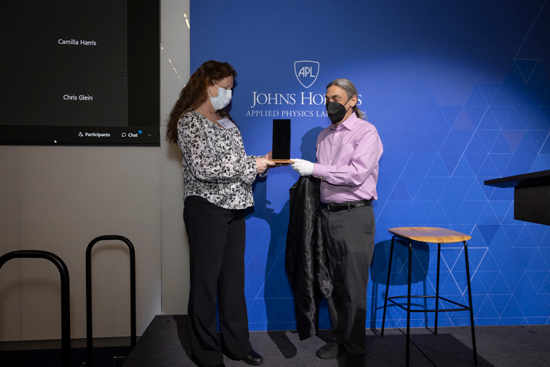 Europa Clipper project scientist on right presents a black, rectangle-shaped award to Karla Clark, a woman standing on the left.
