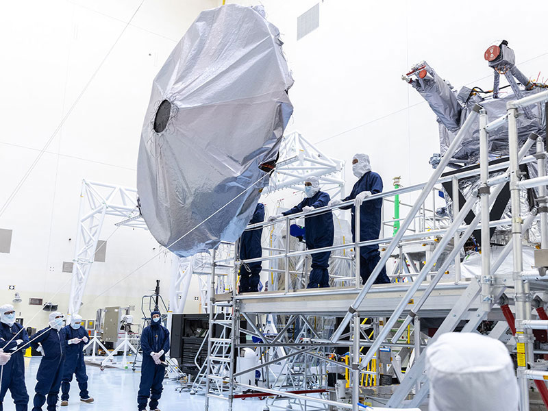 Workers in blue overalls and white head covers guide Europa Clipper's high gain antenna as it's installed on the spacecraft.