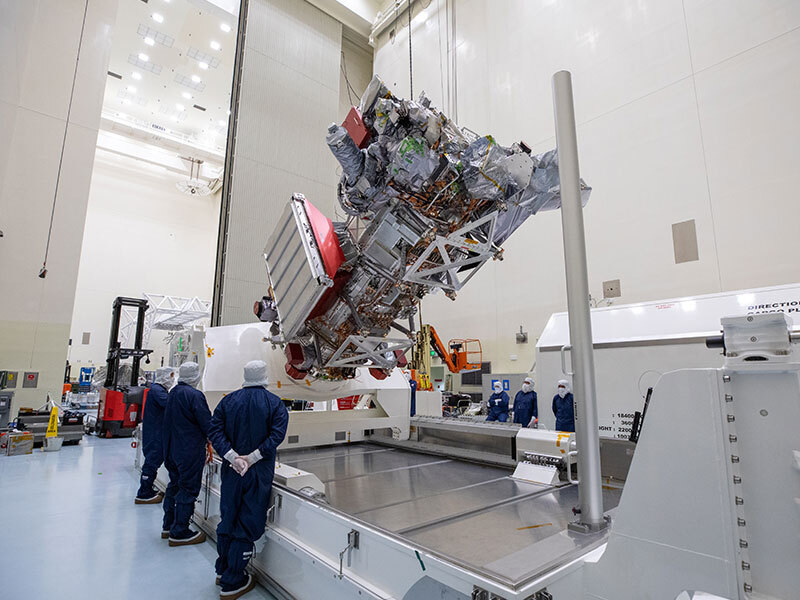 Workers in blue overalls and white head covers watch as equipment is used to rotate Europa Clipper. 