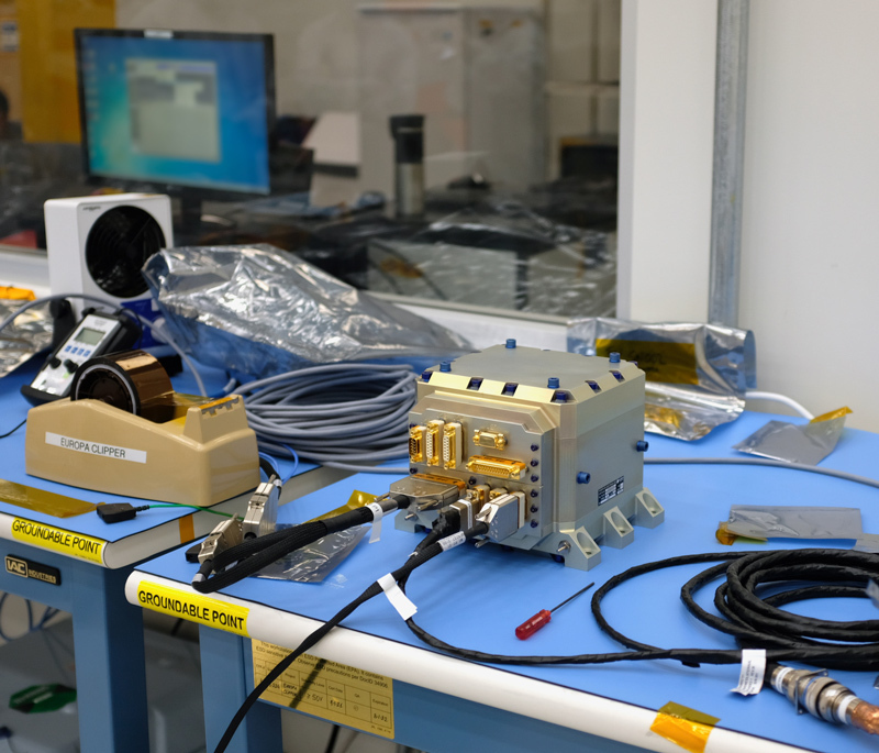 One of Europa Clipper’s star tracker electronics boxes (the bronze-colored cube at center) sits in a JPL clean room for testing in October 2021. After the spacecraft’s launch in October 2024, the star tracker will autonomously identify stars to determine Europa Clipper’s orientation in space. The device is essential for precisely pointing the spacecraft’s science instruments and communication antennas.