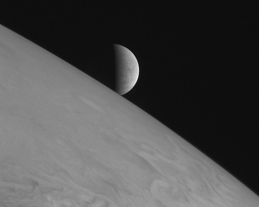 black and white view of half-illuminated moon over curving horizon of large planet