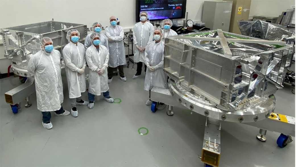 Engineers and technicians in a clean room at NASA's Jet Propulsion Laboratory in Southern California stand between the thick-walled aluminum vault and its duplicate that they helped build for the agency's Europa Clipper spacecraft.