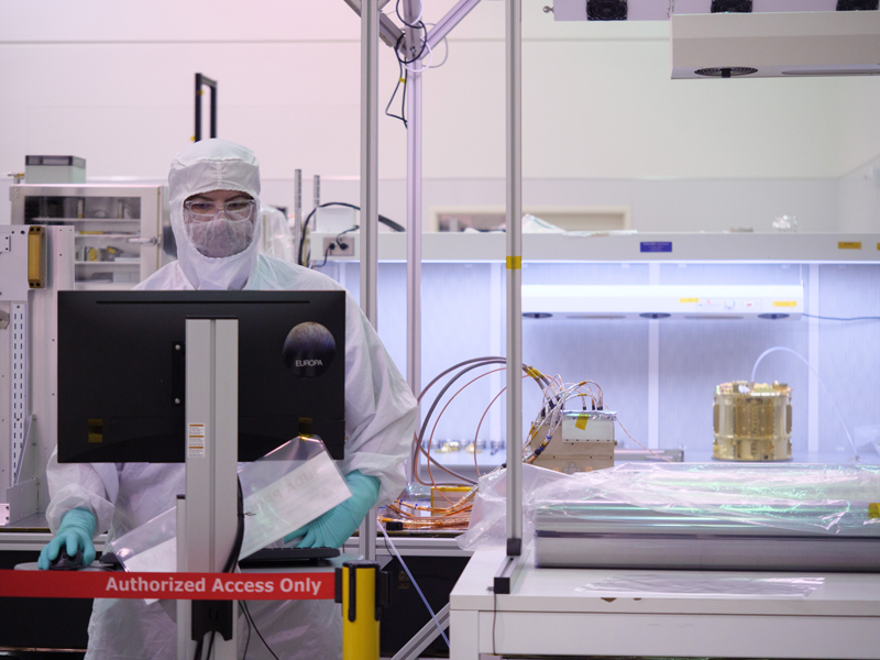 An image showing an engineer testing the SUrface Dust Analyzer (SUDA) electronic box next to the partially assembled instrument in the cleanroom at the Laboratory for Atmospheric and Space Physics (LASP) at the University of Colorado Boulder.